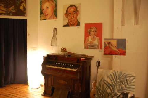 A piano in the corner of a room with paintings on the wall.