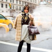 A woman in fur coat and scarf standing on street.