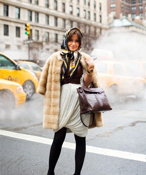 A woman in fur coat and scarf standing on street.
