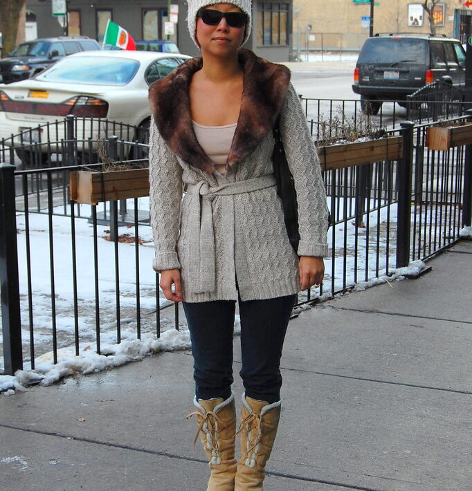 A woman in boots and a jacket on the sidewalk.