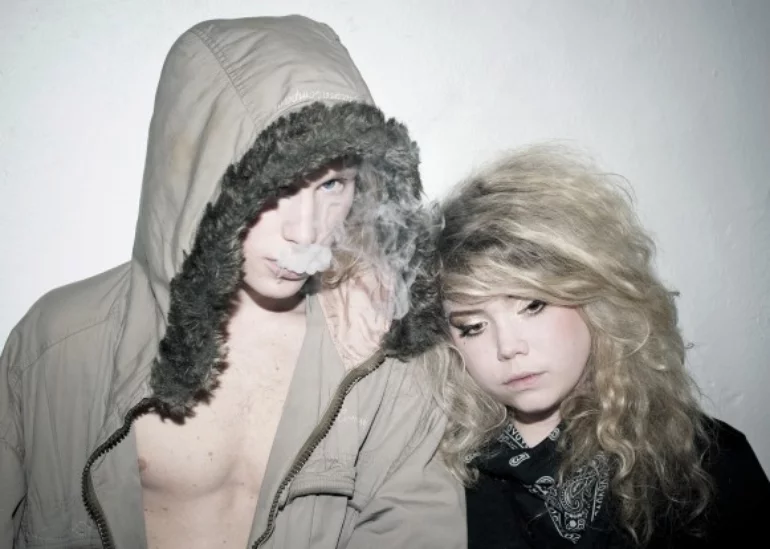 A man and woman smoking in front of a wall.