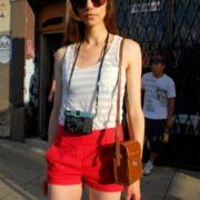 A woman wearing red shorts and sunglasses holding a brown purse.